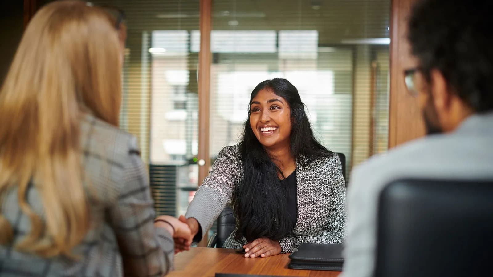 A smiling candidate shaking hands with an interviewer across a meeting-room table