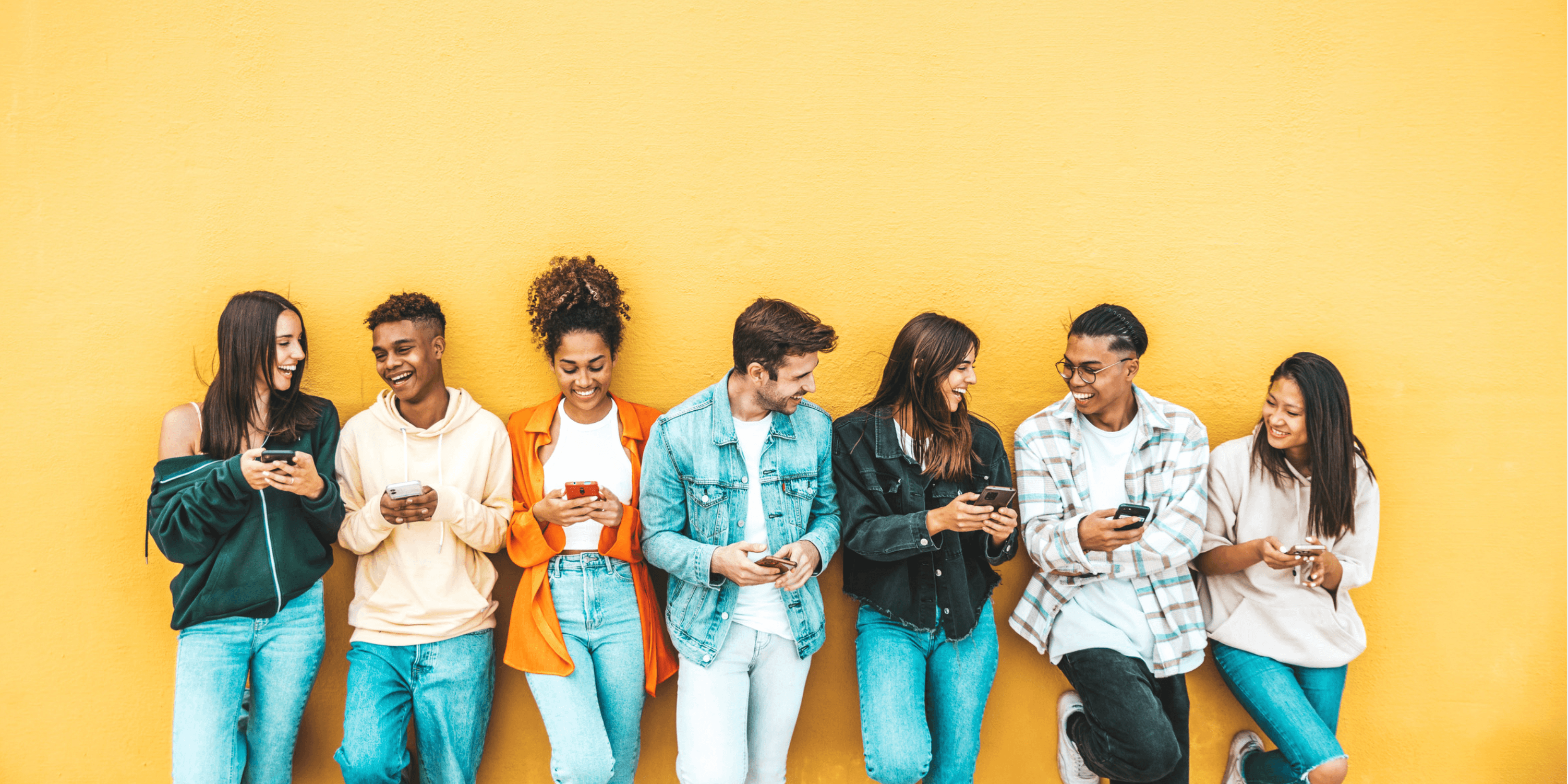 Diverse young adults with smartphones against a bright yellow wall